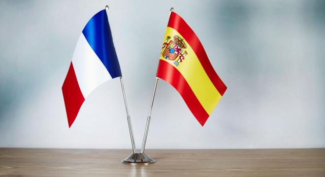 La deducción por doble imposición internacional en el IRPF exige acreditar el pago efectivo de un impuesto similar. Bandera francesa y española de pie sobre una mesa