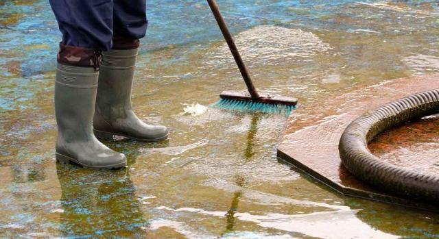 Compensación de los beneficios fiscales en las cuotas del IBI y del IAE, por los daños causados por la DANA. Imagen de un hombre con botas de agua y elementos de limpieza