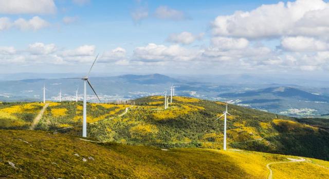 En Galicia se aprueba una deducción en IRPF en relación con proyectos de especial interés público, social y económico y otra deducción en ITP y AJD con la producción de energías renovables. Imagen de un monte gallego con molinos de energia renovables